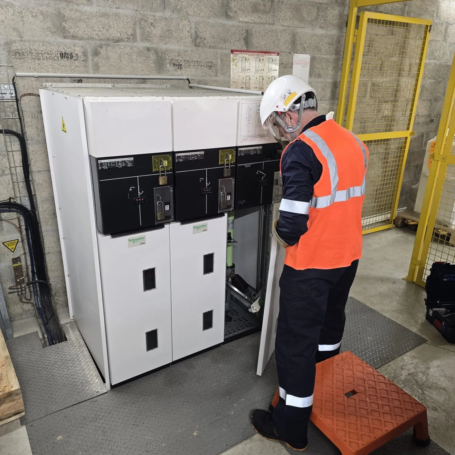 Technicien en tenue de protection contrôlant les cellules HTA d'un poste électrique